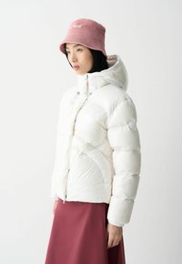 Vit puffjacka med dragkedja fram, huva och texturerade ärmar, kombinerad med en rosa kordflodshatt och en vinröd kjol.