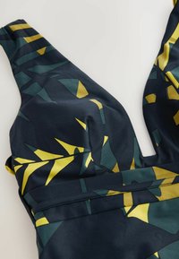 Maillot de bain bleu marine avec un décolleté en V profond, arborant des motifs géométriques abstraits en jaune et vert. Tissu doux et extensible avec une texture lisse.