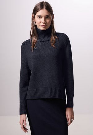 Maglione turtleneck a maglia blu navy con polsini e orlo a costine, dotato di una vestibilità comoda e tessuto testurizzato, abbinato a un vestito coordinato.