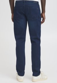 Tumesinised teksapüksid sirge säärega, millel on kaks tagataskut ja siledapind, kombineeritud valgete tennistega.