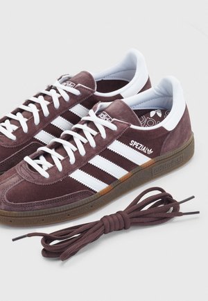 Baskets Adidas Spezial marron avec des bandes et des lacets blancs, accents blancs au talon, et une paire supplémentaire de lacets marron sur fond blanc.