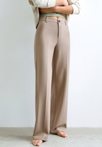 Pantalons beiges à jambe large avec une coupe ajustée, dotés d'une fermeture à bouton à l'avant et d'un minimalisme en matière de couture, fabriqués à partir d'un tissu lisse.