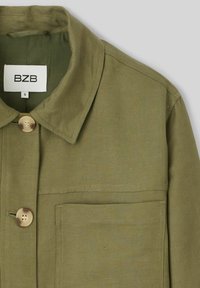 Veste chemise vert olive en tissu texturé, avec un col, une poche frontale et deux boutons beiges. L'étiquette indique "BZB" et taille "S."