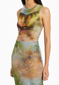 Hame ilman hihnoja, joka esittelee vartalonmyötäistä muotoilua, valmistettu kevyestä, teksturoidsesta kankaasta, jossa on värikäs abstrakti kuvio vihreän ja ruskean sävyissä.