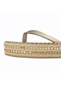 Sandal in corda metallica dorata con base intrecciata color tan, caratterizzata da borchie a piramide dorate lungo i lati. La suola platform aggiunge altezza e texture.
