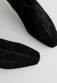 Stivali alla caviglia in suede neri con punta affilata e texture liscia, dotati di un dettagli di cucitura lungo il lato.