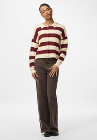 Svītrainais kardigans krēmkrāsā un bordošā ar apkakli, pogām priekšpusē, ribota apdare piedurknēs un brīvs piegriezums. Kombinēts ar brūnām biksēm.