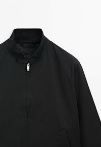 Black jacket with stand-up collar, front zipper, and visible pocket on right side against a white background.