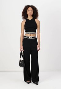 Melnā īsā tank topa kombinācija ar augstiem melniem platājiem biksēm. Iekļauj baltu svītru jostu un teksturētu melnu roku somu.