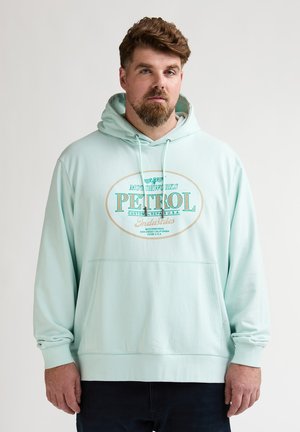 Sweat à capuche bleu sarcelle clair en tissu doux, avec une poche avant et un imprimé graphique avec "PETROL" en lettres grasses.