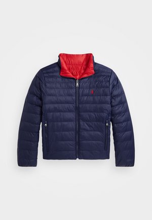 Veste matelassée bleu marine avec col intérieur rouge, fermeture éclair sur le devant, deux poches latérales zippées et petit logo rouge brodé sur la poitrine.