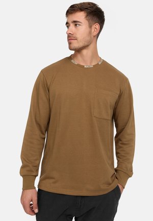 Braunes Langarm-T-Shirt mit rundem Ausschnitt, einem kontrastierenden weißen Markenlabel, einer Brusttasche und gerippten Bündchen.