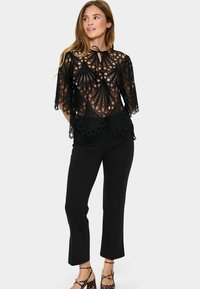 Top in pizzo nero con intricati motivi a rete, maniche corte e collo con lacci arricciato. Abbinato a pantaloni neri aderenti e scarpe con stampa leopardata.