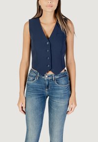 Gilet sans manches bleu marine avec un décolleté en V profond, six boutons sur le devant et une poche poitrine unique. Associé à un jean bleu.