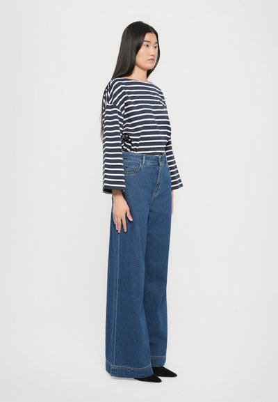 Maglia a righe a maniche lunghe in blu e bianco, abbinata a jeans blu a vita alta e a gamba larga. Il tessuto sembra morbido; i jeans hanno una vestibilità rilassata.