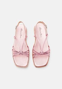 Une paire de sandales ouvertes en métal rose avec des avant-pieds carrés, des straps noués, des boucles à la cheville et des bords décoratifs perlés sur fond blanc.