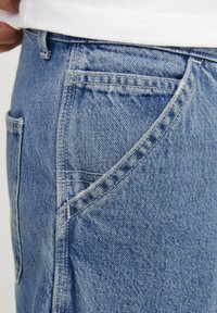 Jeans de mezclilla azul claro con un corte relajado, que incluyen bolsillos laterales y traseros, costuras visibles y una textura de tela suave.