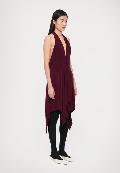 Rochie fără mâneci mov pal, cu decolteu adânc în V, decorată cu pliuri drapate și tiv asimetric. Asortată cu ciorapi negri și mule albe.