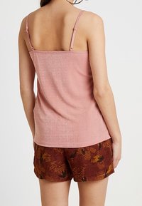 Haut sans manches rose clair avec de fines bretelles ; tissu texturé. Associé avec un short marron présentant un motif floral coloré.