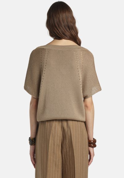 Femme aux longs cheveux bruns portant un haut en maille marron clair à manches courtes et amples, et un pantalon marron à rayures fines taille haute, vue de dos.