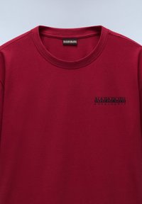 Camiseta burdeos con cuello redondo, mangas cortas y un logo negro impreso en el lado izquierdo del pecho. Fabricada con material de algodón suave y liso.