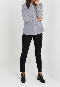 Chemise à rayures blanches et bleu marine à manches longues, associée à un pantalon slim noir et des chaussures à talons noires.