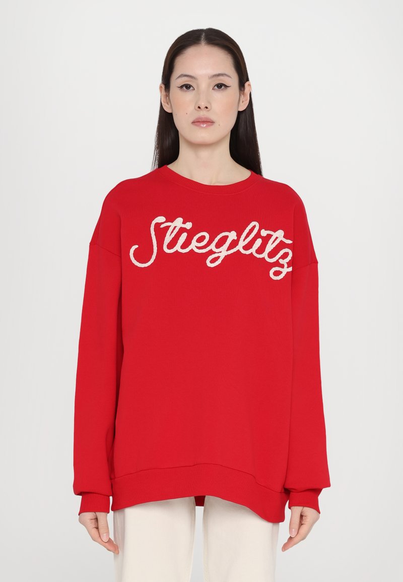 Sudadera roja con cuello redondo, que presenta un texto en relieve blanco "Stieglitz" en la parte frontal y mangas de corte holgado.