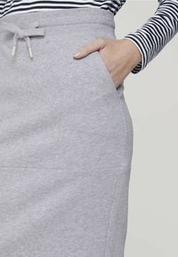 Jupe en coton gris avec une taille élastique et un cordon de serrage. Dispose de poches latérales et d'une texture lisse. Détails de couture décoratifs visibles.