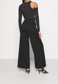 Czarny bodysuit z długim rękawem i odkrytymi ramionami, zestawiony z czarnymi spodniami z wysokim stanem o szerokich nogawkach. Charakteryzuje się gładką teksturą i dopasowanym krojem.