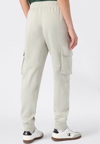 Hellgraue Cargo-Hosen mit seitlichen Taschen und gerippten Bündchen, aus weichem Stoff gefertigt. Kombiniert mit weißen Sneakers mit schwarzen Akzenten.