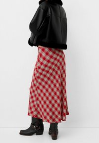 Czarna kurtka crop top z ekoskóry w połączeniu z czerwoną długą spódnicą w kratę, z białymi i czarnymi wzorami w kratkę. Czarne botki za kostkę z ozdobnymi klamrami.