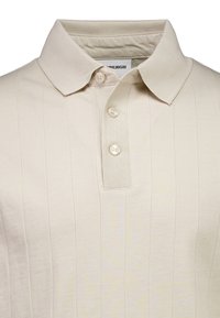 Beiges Poloshirt mit geripptem Kragen, ausgestatte mit einer Knopfleiste und vertikaler Rippenstruktur im gesamten Stoff. Weiches Baumwollmaterial.