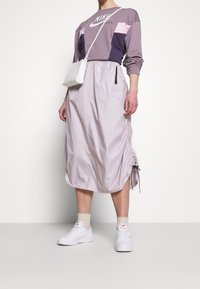 Ljuslavendelkjol med gatherade sidor och dragsko, kombinerad med en lila och rosa Nike-tröja, vita sneakers och en liten väska.