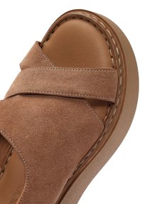 Sandal in suede marrone a scivolo con cinturini incrociati, soletta imbottita e suola leggera e testurizzata con cuciture a vista.