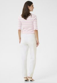Top de rayas en rosa y blanco con mangas hasta el codo y dobladillos con volantes, combinado con jeans rectos blancos y sandalias de tacón alto beige.