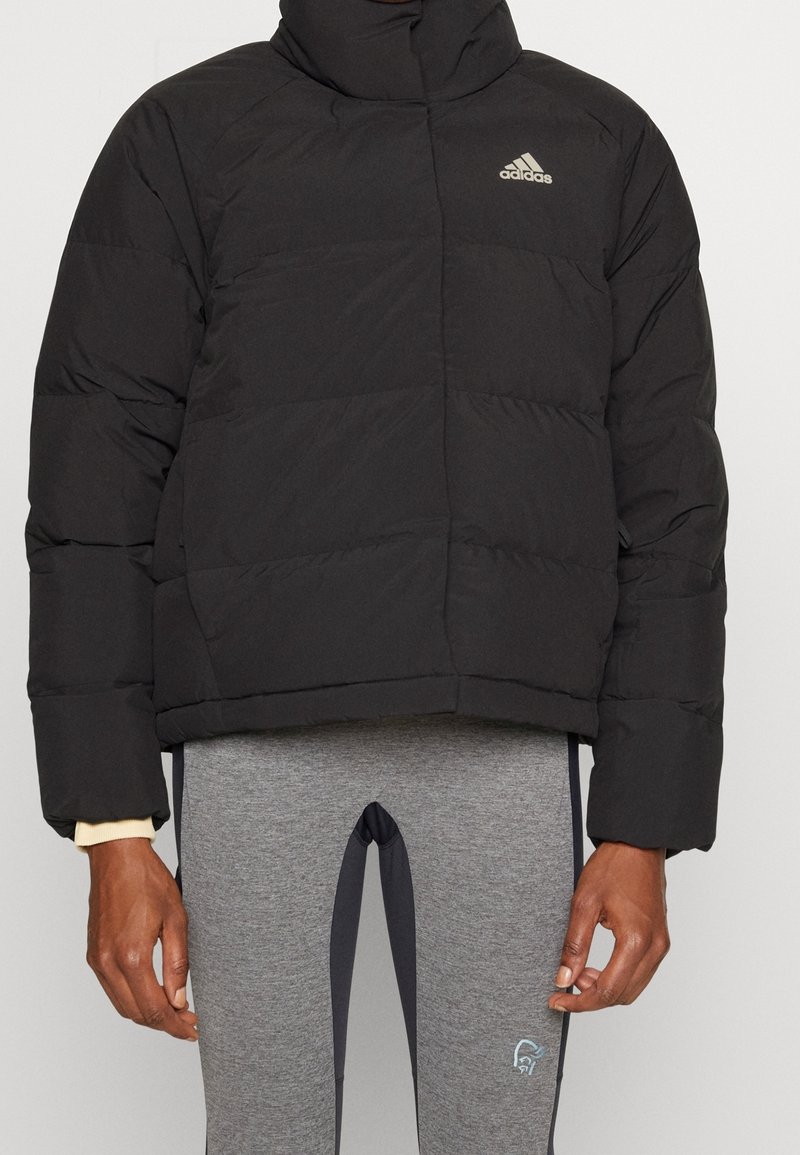 Svart puffjacka med hög krage, quiltad textur och broderad logo på vänster bröst. Matchad med grå träningsleggings.