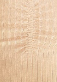 Tessuto beige a coste con strisce verticali e texture arricciata al centro. Il materiale appare morbido con una leggera lucentezza.