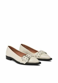 Ballerines en cuir blanc avec un bout pointu, dotées d'une boucle argentée proéminente et d'accents de clous sur le dessus. Semelle noire. Texture lisse.