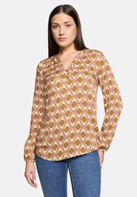 Blusa a maniche lunghe con scollatura a V, caratterizzata da un motivo floreale in tonalità di marrone, arancione e crema su uno sfondo chiaro.