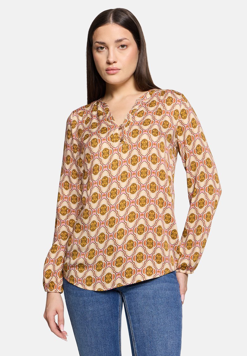 Blusa a maniche lunghe con scollatura a V, caratterizzata da un motivo floreale in tonalità di marrone, arancione e crema su uno sfondo chiaro.