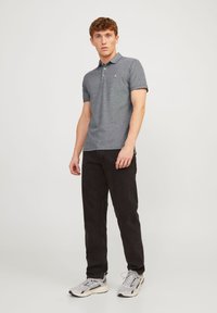 Gray polo shirt with short sleeves, three-button placket, and small logo detail, paired with black pants and gray athletic shoes.