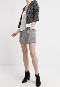 Černobílá krátká bunda s texturovanou látkou, v kombinaci s bermudami s geometrickými tvary a černými kotníkovými botami.