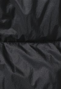 Zwarte pufferjas stof, matte textuur met een licht kreukelige uitstraling, heeft gestikte secties en een gladde afwerking.