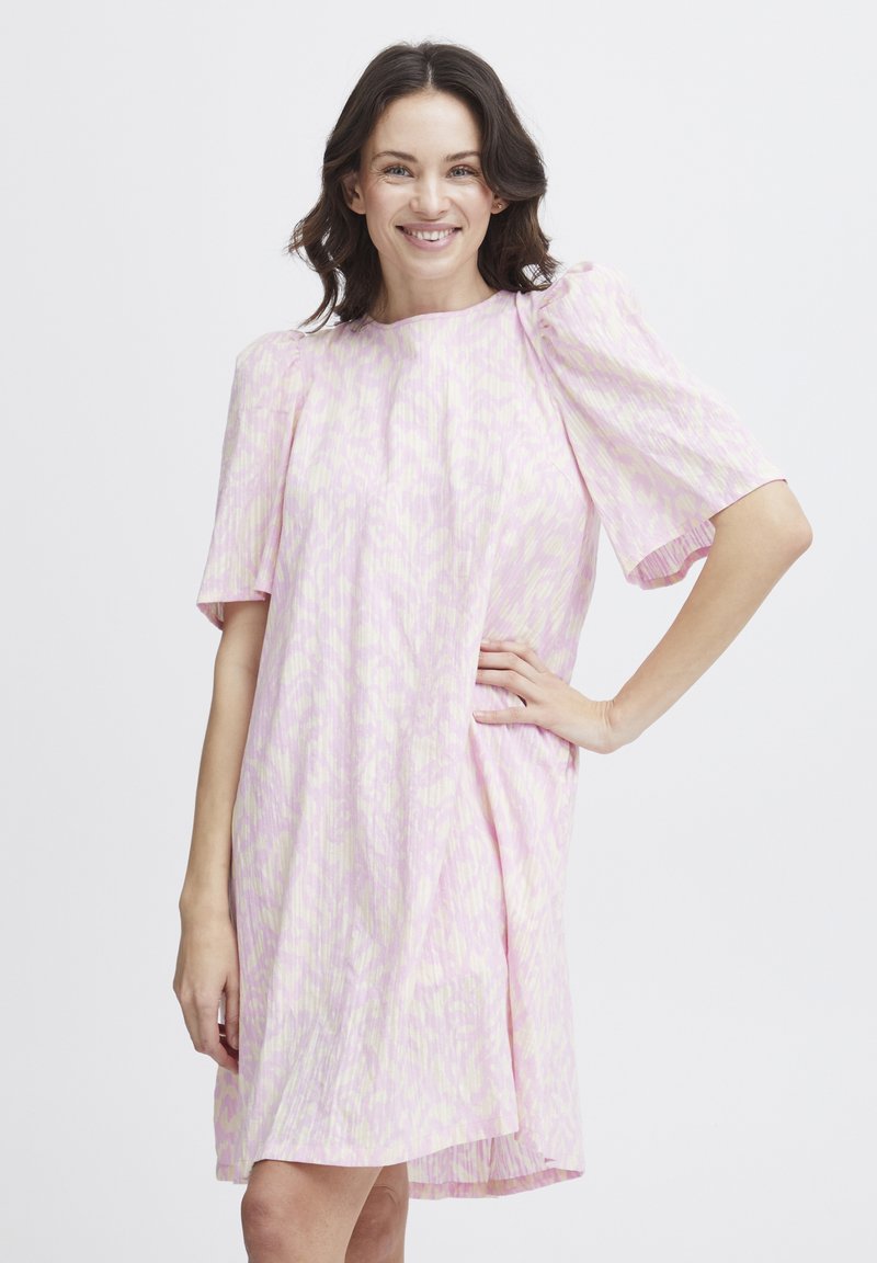 Vaaleanpunainen mekko, jossa on lyhyet puffihihi ja rento istuvuus. Siinä on hillitty abstrakti kuvio ja se ulottuu polvien ylle. Silkkinen rakenne.