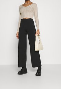 Un haut cropped beige à côtes, un pantalon large noir, des bottes noires à lacets, et un sac à main texturé blanc cassé. Éléments de design simples et modernes.