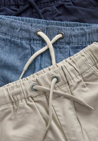 Tre par shorts stablet: mørk navy, lys blå denim og beige bomuld. Hver har et elastisk taljebånd og snor.