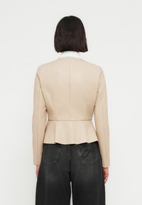 Μπεζ σακάκι peplum με εφαρμοστό σχέδιο και λευκό γιακά. Λείο, ραμμένο ύφασμα· συνδυασμένο με σκούρο, φαρδύ τζιν παντελόνι.