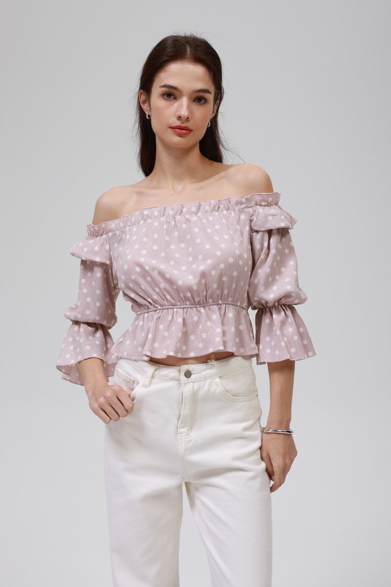 Haut rose pâle à épaules dénudées avec des pois blancs, des manches volantes et un ourlet évasé ; associé à un pantalon blanc taille haute.