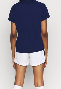 Mörkblå idrottströja med korta ärmar och en lätt höga-låga fåll, matchad med vita shorts med en svart sidolist.