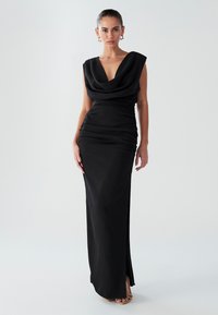 Abito lungo nero con scollatura drappeggiata, silhouette aderente e dettagli arricciati ai lati. Tessuto liscio con uno spacco alto fino alla coscia.